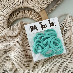 Close-up of mint green elastic hair ties set in clear packaging on a straw bag