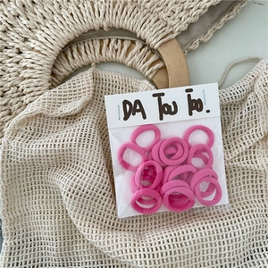 Close-up of pink elastic hair ties in a clear bag with paper header on woven texture