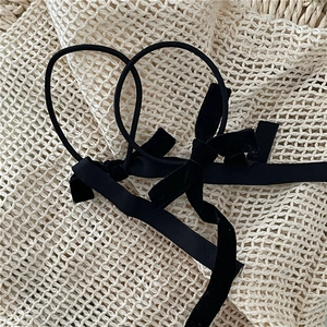 Detail view of two black velvet ribbon bow hair ties on a minimalist textured background