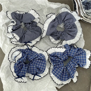 Close-up of four blue plaid fabric scrunchies with white ruffles and small bows