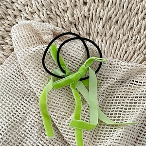 Detailed macro view of avocado green velvet bow hair ties on a rustic woven mat background