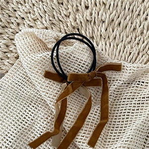 Detail of caramel velvet hair scrunchie with long ribbon bow on white mesh fabric