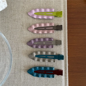 Dettaglio di cinque fermagli per capelli ondulati in metallo dai colori Morandi su lino