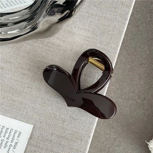 Detail view of burgundy heart-shaped hair claw clip with golden metal spring on fabric