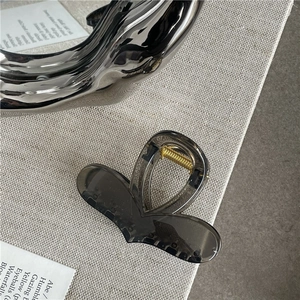 Detail view of a translucent charcoal hair claw clip with golden spring and silver accessory