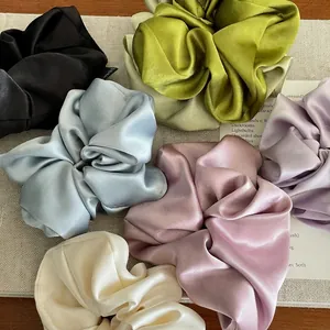 Elegant satin silk scrunchies in multiple colors displayed on a beige woven background