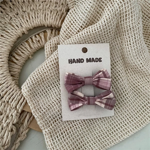 Close-up of handmade pink checkered bow hair clips on a card with woven background