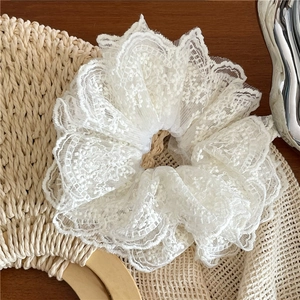 Détail d'un chouchou en dentelle blanche avec broderie florale sur un sac en paille