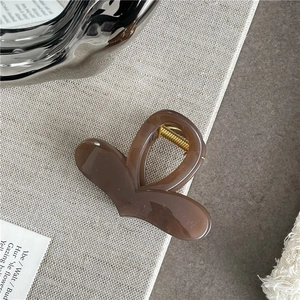 Macro detail of heart-shaped hair claw with coffee amber marble texture and gold spring