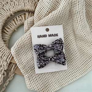 Close-up of two handmade floral fabric bow hair clips on a white display card