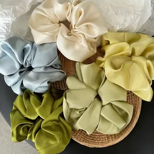 Set of five colorful premium satin hair scrunchies on a textured woven background