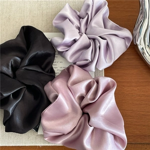 Detailed view of three satin silk scrunchies in black, lilac, and dusty pink colors