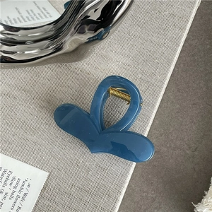 Close-up of a blue heart-shaped hair claw clip with glossy jelly texture and gold spring