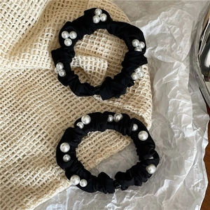 Detail of black satin hair scrunchies with elegant white faux pearls on soft fabric