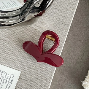 Macro detail of glossy burgundy heart hair claw clip with golden spring on silver tray