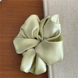 Macro shot of the light green satin hair scrunchie showing glossy fabric texture