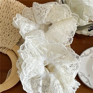 Détail d'un chouchou en dentelle blanche avec broderie florale sur fond en bois