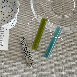 Detail of three colorful acetate geometric hair clips on a linen fabric background