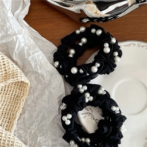 Close-up of black fabric hair scrunchies with white faux pearl beads on a wooden desk
