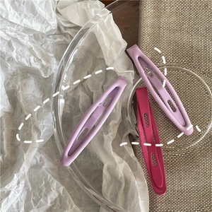 Detail of lavender and rose red oval hollow metal hair clips on a glass container edge