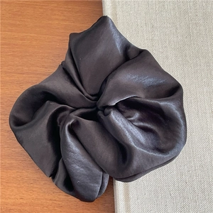 Detail shot of oversized dark satin scrunchie with glossy texture on a book corner