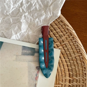 Dettaglio del fermaglio per capelli a goccia d'acqua ondulato rosso scuro e blu-verde