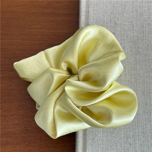 Close-up of premium satin scrunchie in cream yellow with elegant silk texture
