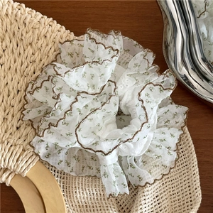Détail d'un chouchou en dentelle blanche avec broderies de fleurs vertes et bords festonnés