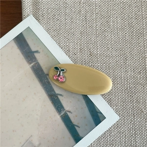 Détail de la pince à cheveux ovale jaune moutarde avec cerise en strass rose et feuille