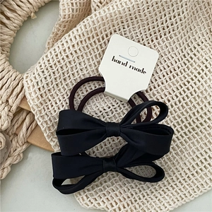Detail of black bow hair scrunchies with handmade labels on a rustic beige background