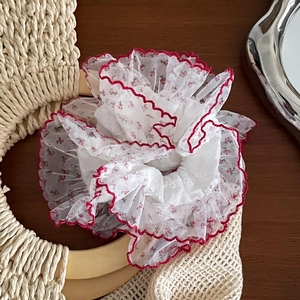 Détail d'un chouchou en organza blanc avec broderie florale rouge et bordure en dentelle