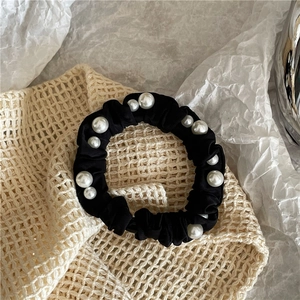 Close-up of black satin scrunchie with white imitation pearls on beige background