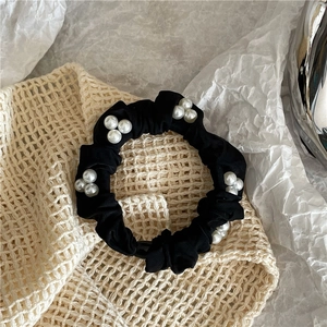 Detail of black fabric scrunchie with clustered white pearls and elegant texture