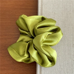 Detailed view of the olive green satin scrunchie with silky texture on wooden surface