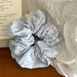 Detailed view of light blue striped scrunchie with floral embroidery on wooden table
