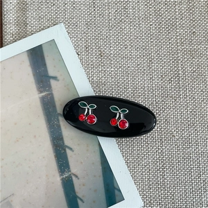 Détail d'une pince à cheveux ovale noire avec des cerises en strass rouges et feuilles vertes