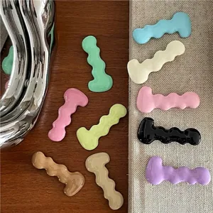 Colorful wavy caterpillar hair clips in various candy colors on a minimal wood background