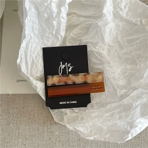 Detail view of two geometric acetate hair clips in amber and marble patterns on card
