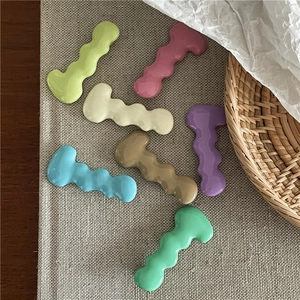 Detail of seven colorful wavy metal hair clips on a textured grey fabric background