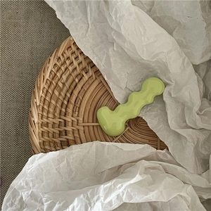 Close-up of a light green wavy caterpillar hair clip on a natural woven rattan tray