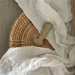 Close-up of Morandi beige caterpillar wave hair clip on a textured woven tray background