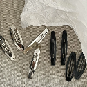 Gros plan de barrettes minimalistes en métal argenté et noir mat sur fond de tissu gris