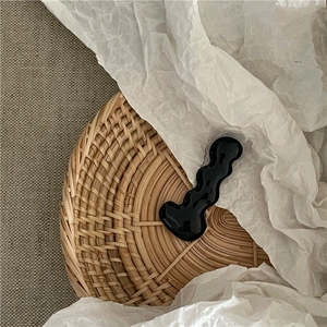 Macro view of glossy black wave-shaped hair clip on an artistic textured paper background