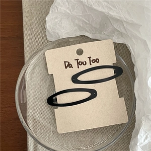 Détail d'une paire de barrettes ovales noires mates présentées sur une carte crème