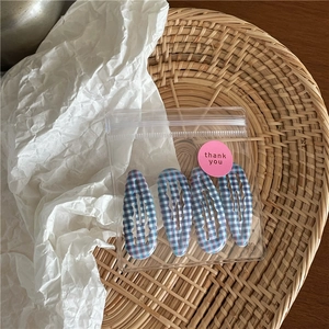 Détail de 4 barrettes à carreaux bleus dans un sac cadeau sur un plateau en osier