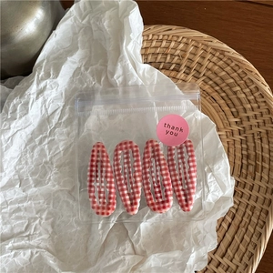Détail de quatre barrettes BB à motif vichy rouge et blanc présentées dans leur sachet