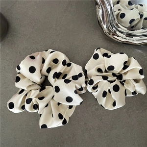 Close-up of elegant black and white polka dot satin hair scrunchies on a stone surface