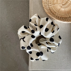 Close-up of premium satin polka dot scrunchie on a beige fabric background