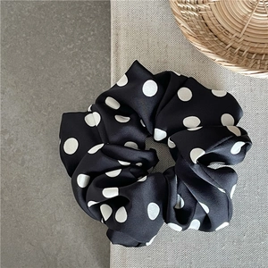 Close-up of black satin scrunchie with white polka dots on a stylish textured background