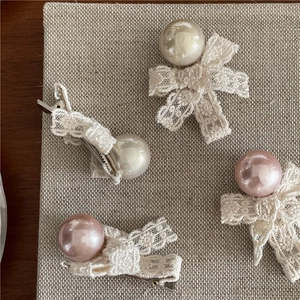 Detailed view of lace bow hair clips with faux pearls in cream white and dusty pink colors